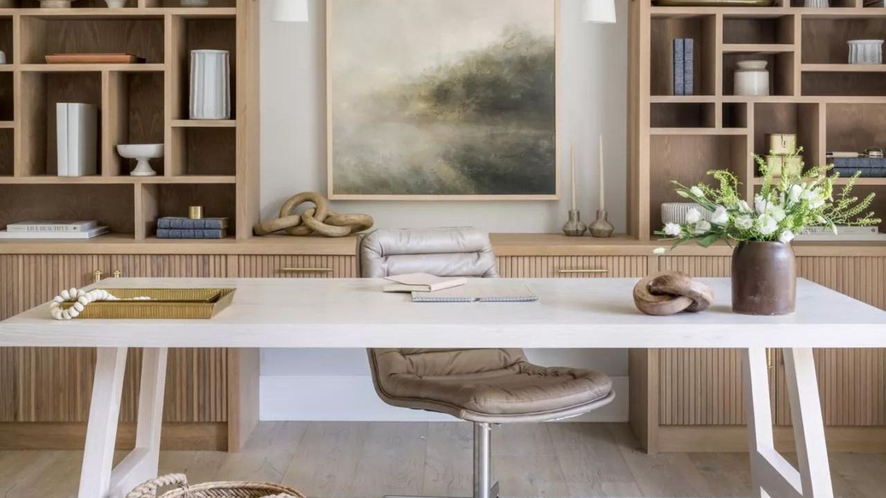 Home office with desk and chair in front of light wood bookshelves