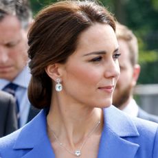 Kate Middleton wearing a blue coat and blue topaz earrings looking to the right