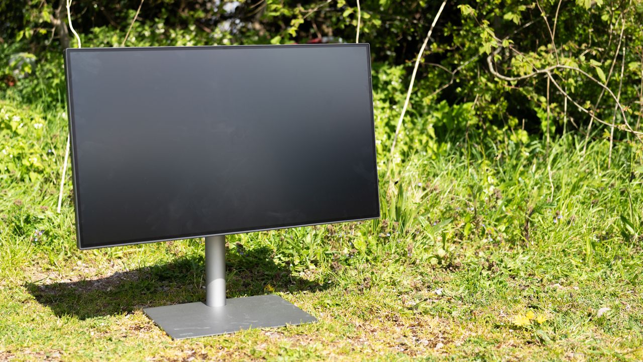 A black BenQ PD3225U monitor sitting on grass in sunshine