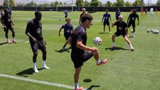 A series of men in uniforms juggle soccer balls on a green turf.