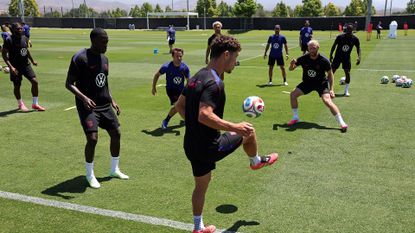 A series of men in uniforms juggle soccer balls on a green turf.