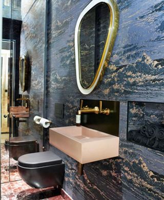 A dark powder room with a black toilet, a pink sink and dark wallpapered walls
