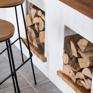 White kitchen island with wooden counter top and alcoves for logs, wood and black metal stools