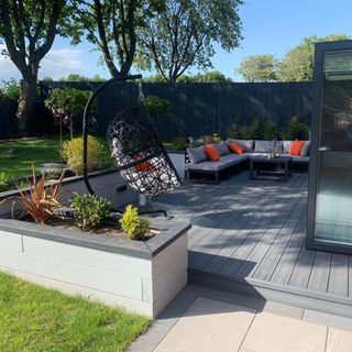 Grey composite decking area in garden with corner sofa and egg chair