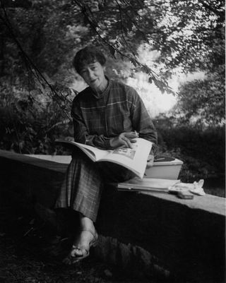 Portrait of American photographer Consuelo Kanaga (1894 - 1978) as she sits outdoors, an open book in her lap, California, 1950s