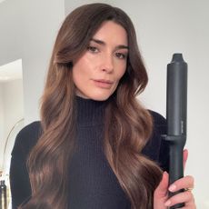 A selfie of Eleanor with loose waves hairstyle, holding GHD Max Chronos Curve curling wand