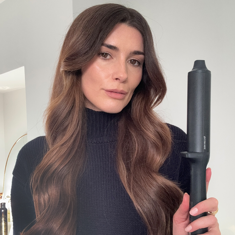 A selfie of Eleanor with loose waves hairstyle, holding GHD Max Chronos Curve curling wand