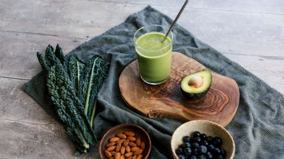 a green smoothie and smoothie ingredients on a tablecloth, on a table