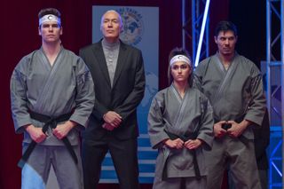 a coach in a suit and three karate athletes at a competition in cobra kai season 6 part 3