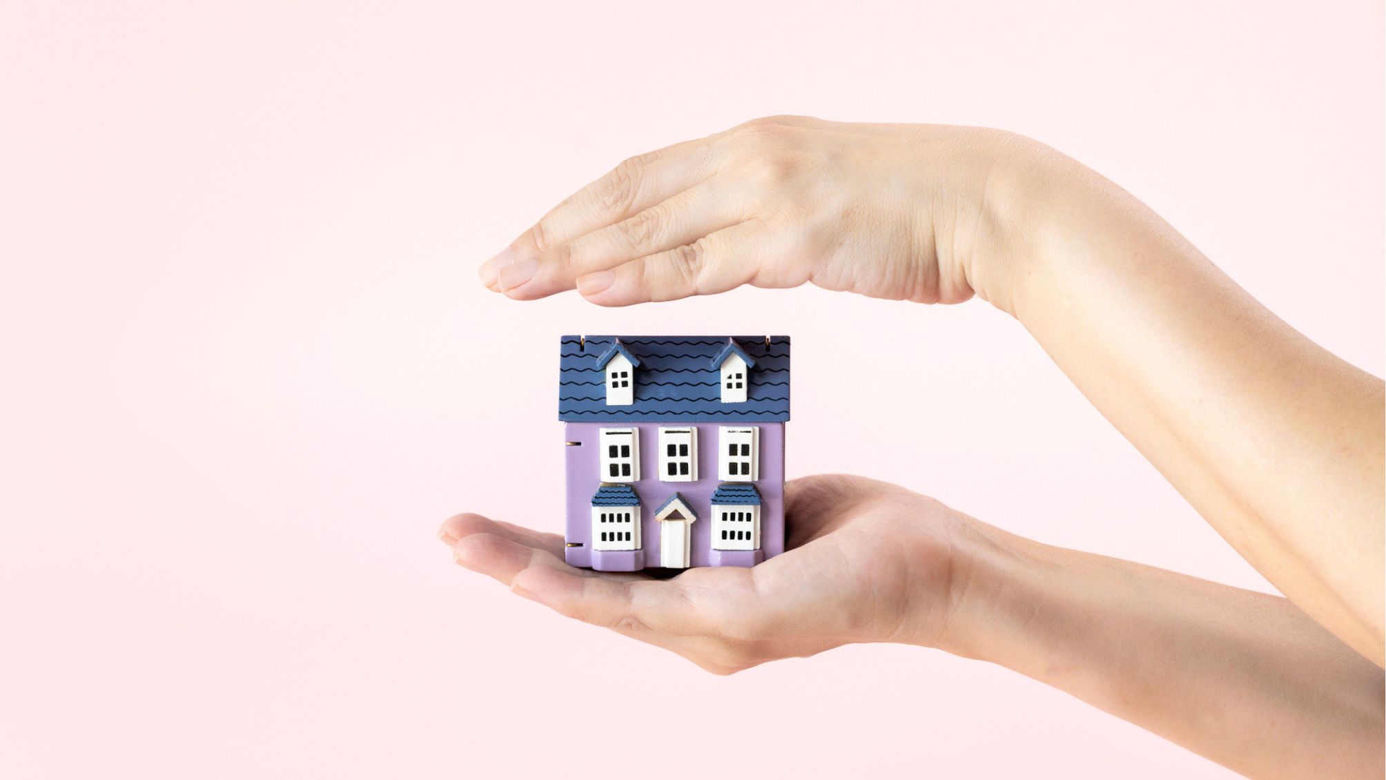 Hands covering a model house on pink colour background.