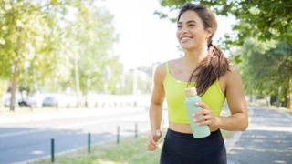a photo of a woman jogging outside with a bottle of water in one hand