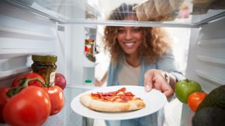 A woman storing leftover pizza in a refrigerator