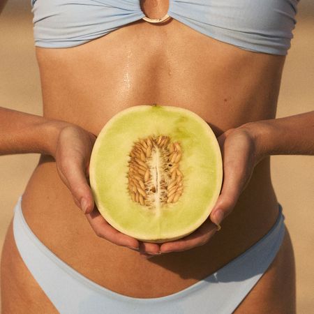 A woman on the beach, in a bikini, eating some fruit