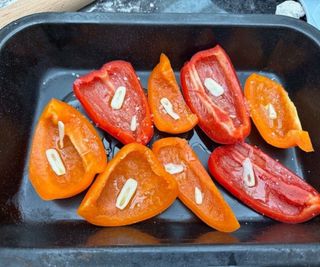 Peppers with a drizzle of oil and cloves of garlic in a cast iron pan.