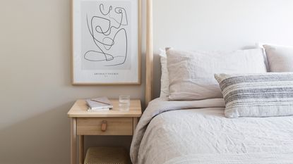 Neutral bedoom with wooden bed and white bedding, wooden bedside table and artwork