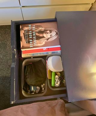 Bedside drawer after very neat with a pile of books on one side and a couple of plastic containers with neat assortment of items including sleep mask and medicine