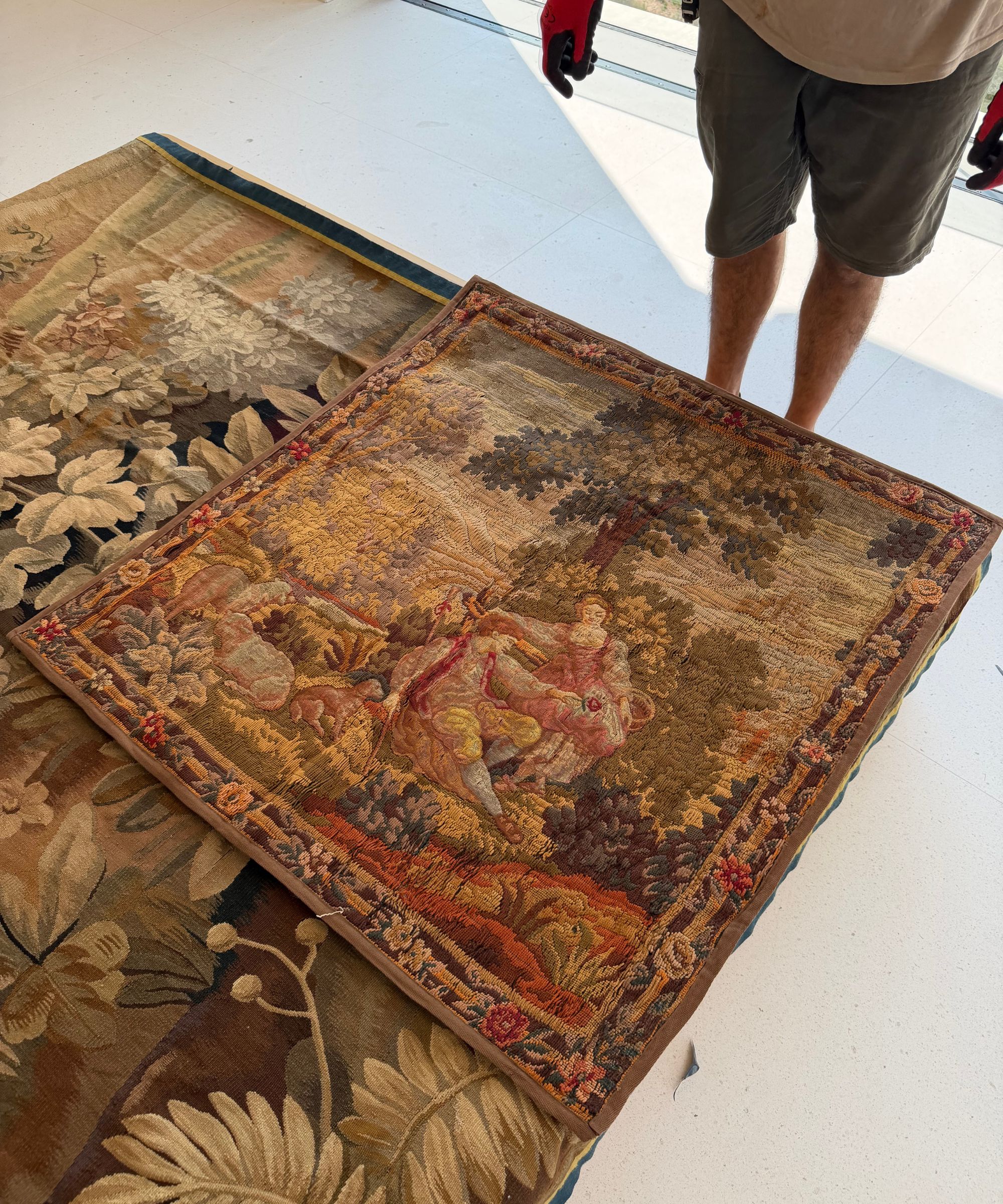Two vintage tapestries on top of one another on the floor