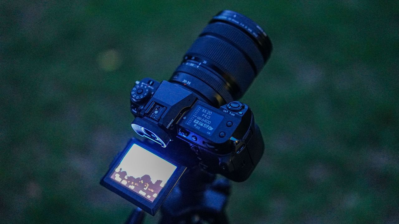 The Fujifilm GFX100S II with the Fujifilm GF 20-35mm f/4 R WR lens attached with the LCD screen extended and glowing, with grass in the background.