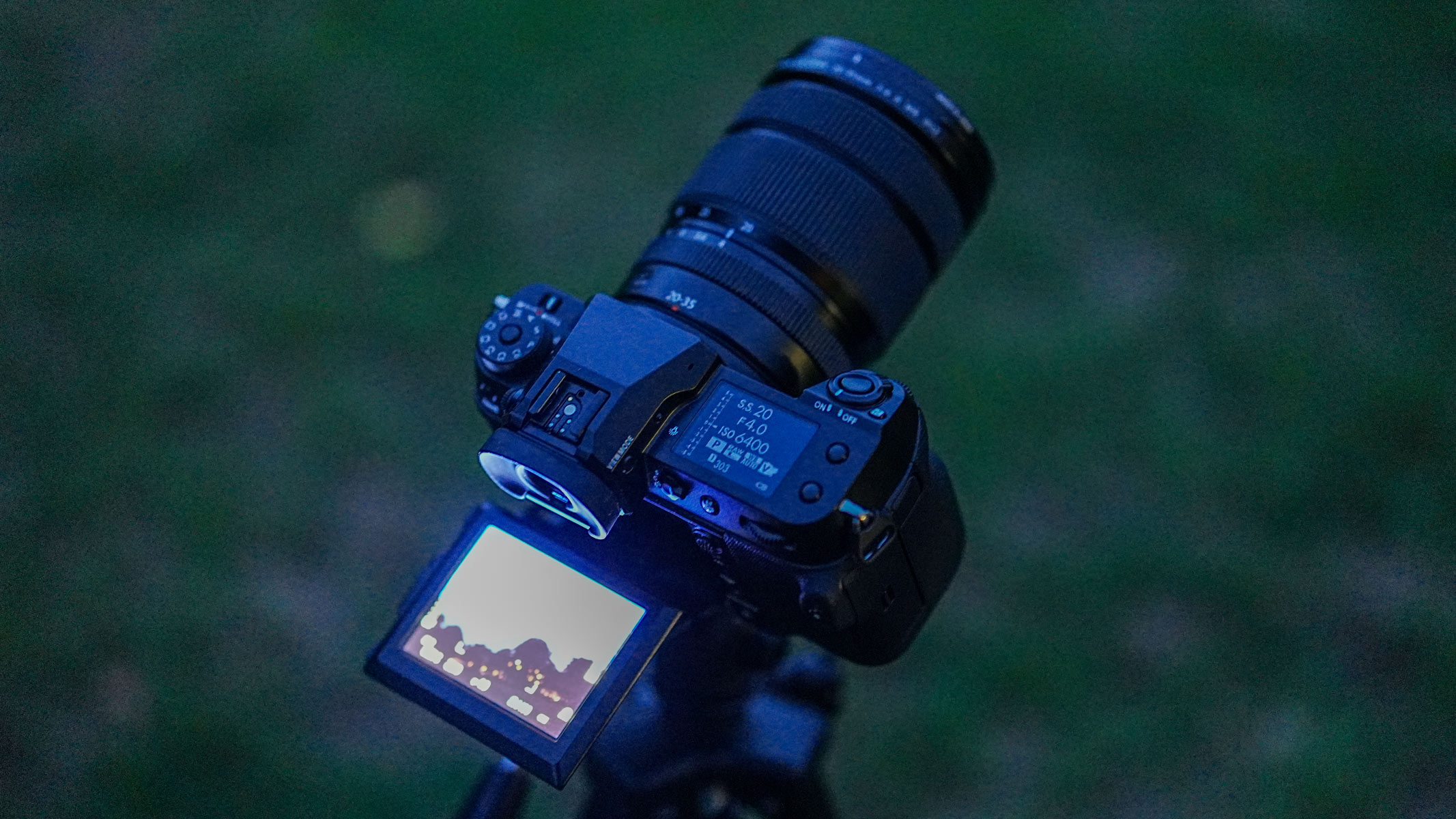 The Fujifilm GFX100S II with the Fujifilm GF 20-35mm f/4 R WR lens attached with the LCD screen extended and glowing, with grass in the background.