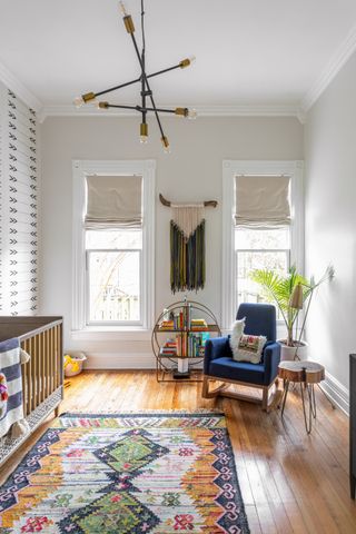 boho style nursery with patterned rug, wallpaper, cot, retro pendant night, blinds, macrame, blue rocking chair