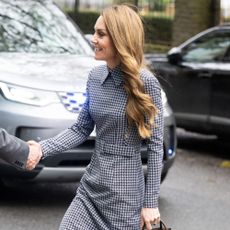Kate Middleton steps outside in London wearing a houndstooth dress with a brown suede DeMellier bag and grey croc-print heels.
