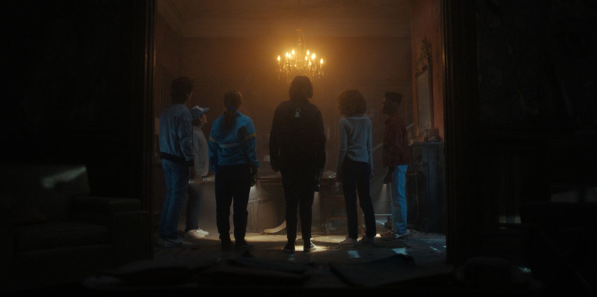 The kids in a Creel House room lit by a chandelier in an official image from Stranger Things season 4