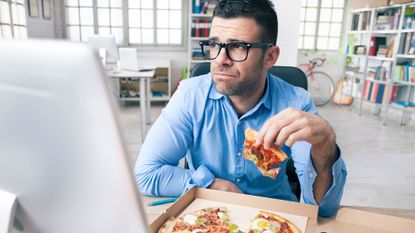 Unhappy man eating pizza at his computer, illustrating that diet changes can make all the difference when it comes to how we look and feel