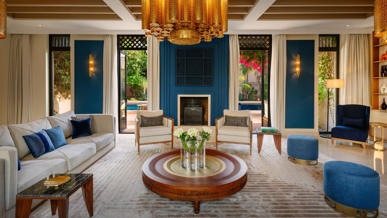 Image of a blue and white, large living room with a white sofa, white accent chairs, and two blue poufs.