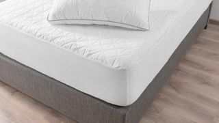 Image shows the corner of a white innerspring mattress on a grey traditional box spring