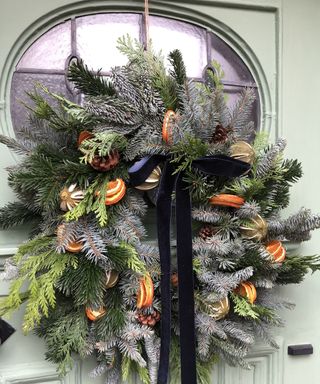 Festive wreath with dried oranges and navy velvet ribbon on green door