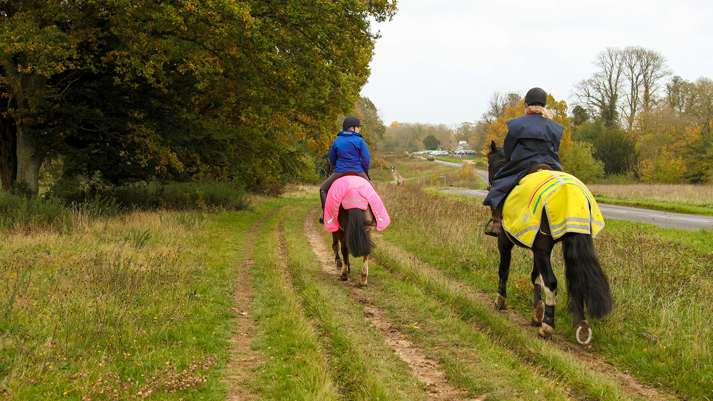 Two horse riders hacking horses on bridleway wearing hi-viz
