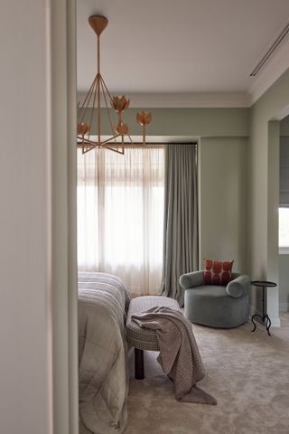 A bedroom with sage green walls, a dark green chair, and gray bedding plus carpet