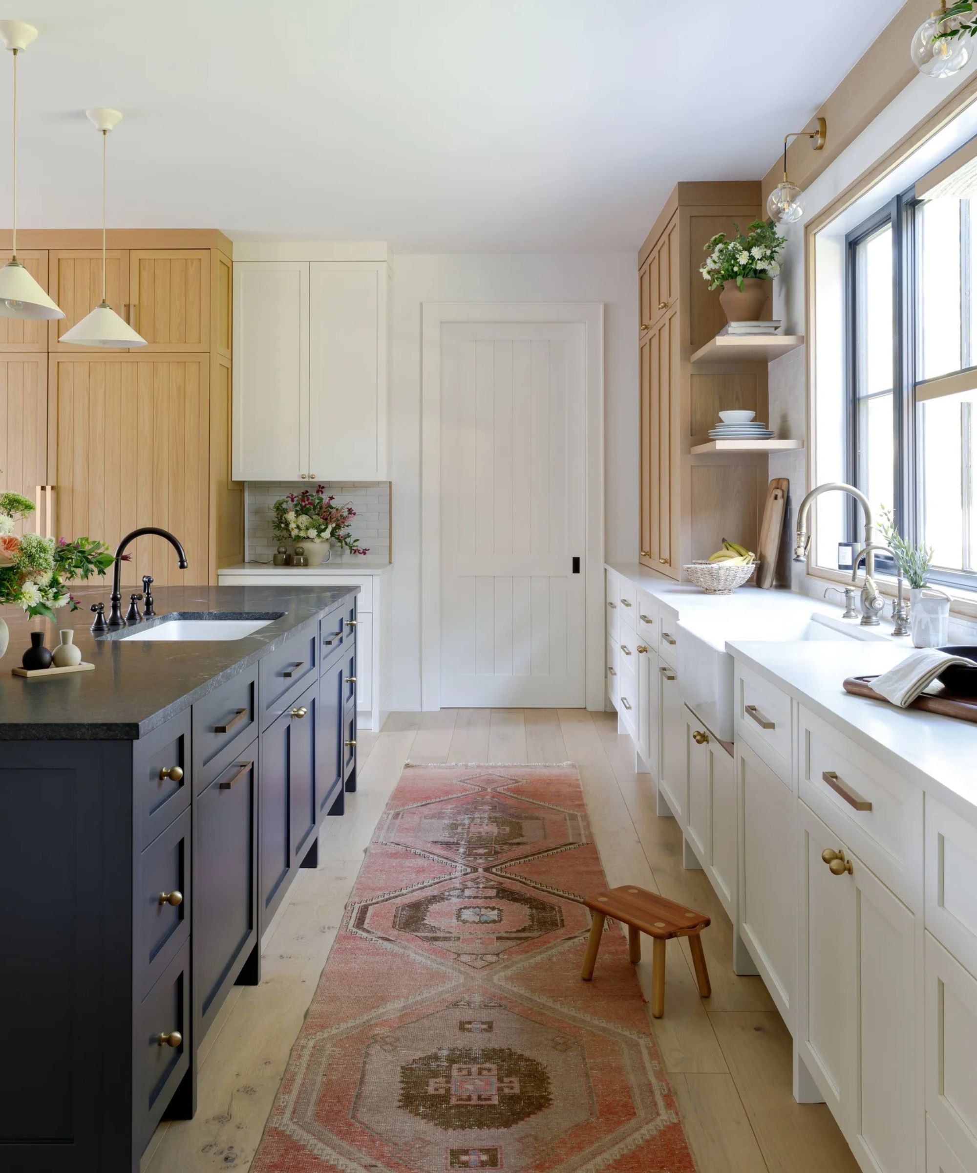 A kitchen with white perimeter cabinets, wood natural oak full-length cabinetry and a dark blue island