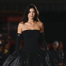 Kylie Jenner walks the Coperni runway wearing a strapless drop waist ball gown with black opera gloves