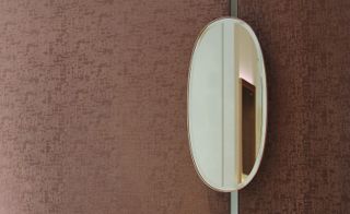An oval mirror against a patterned wall