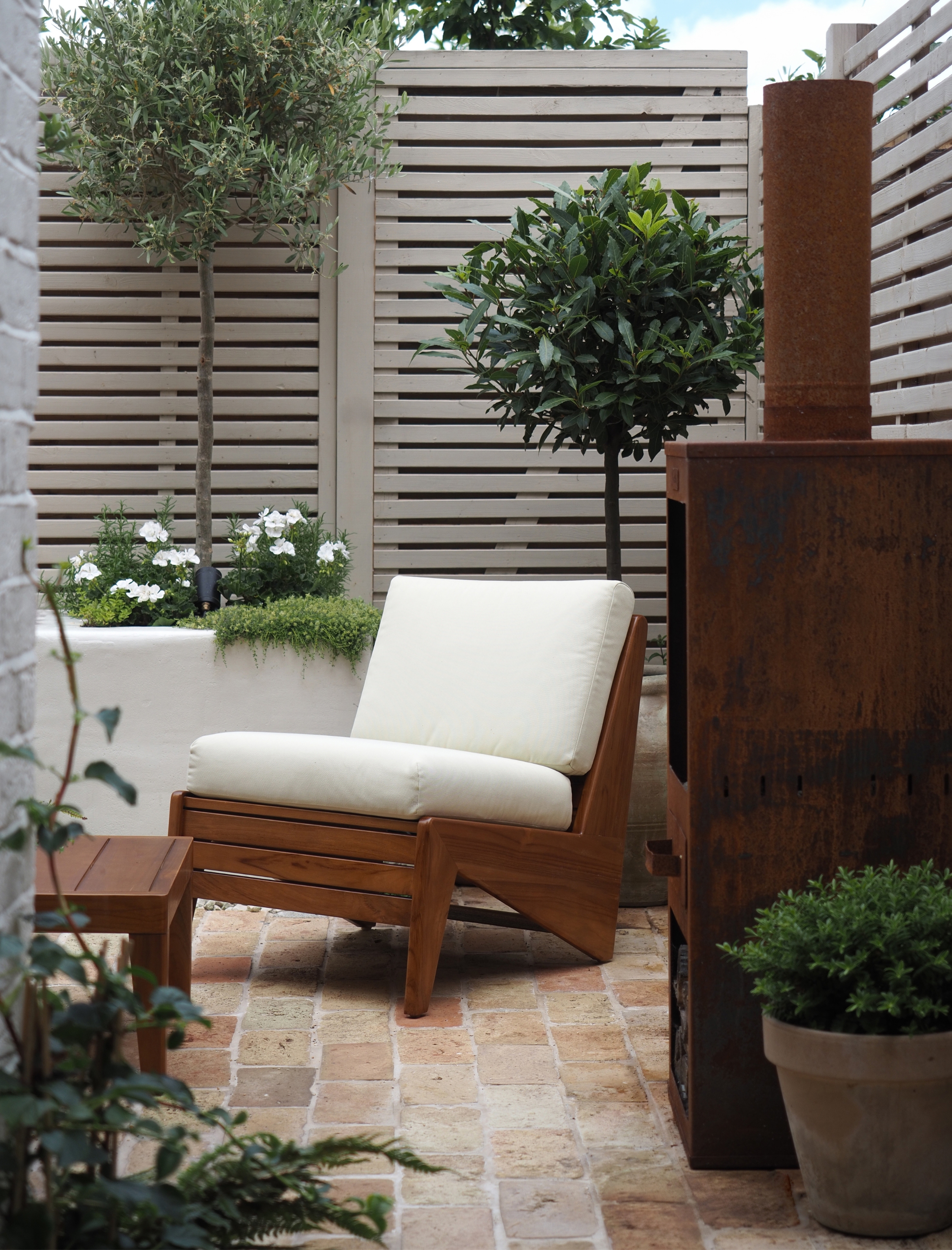 a small mediterranean garden with a brick floor and slatted modern fence