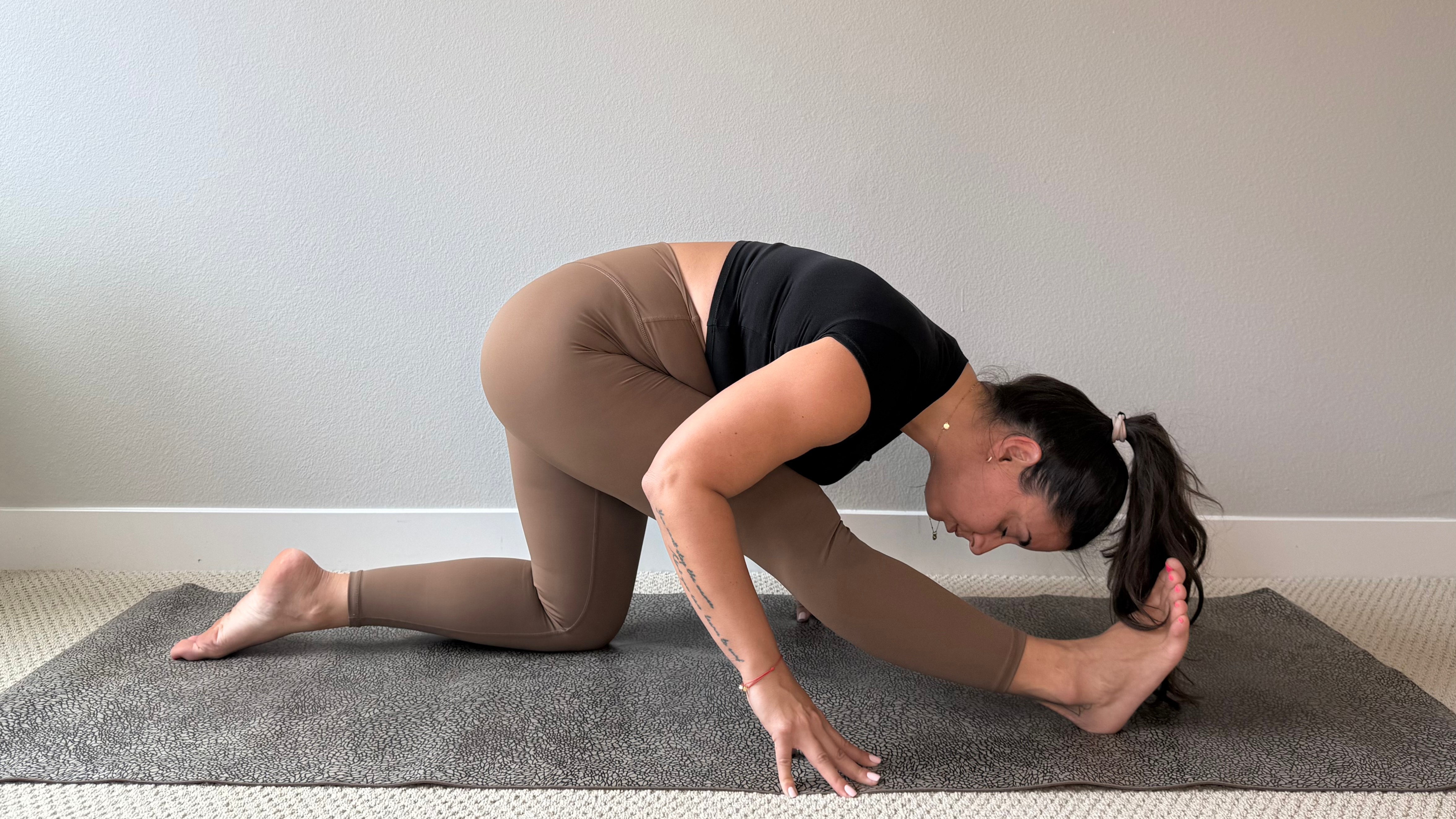 Elma Panagaki performs a half split. She is kneeling on her left leg, with her right leg extended in front of her and her torso bent over her right knee.