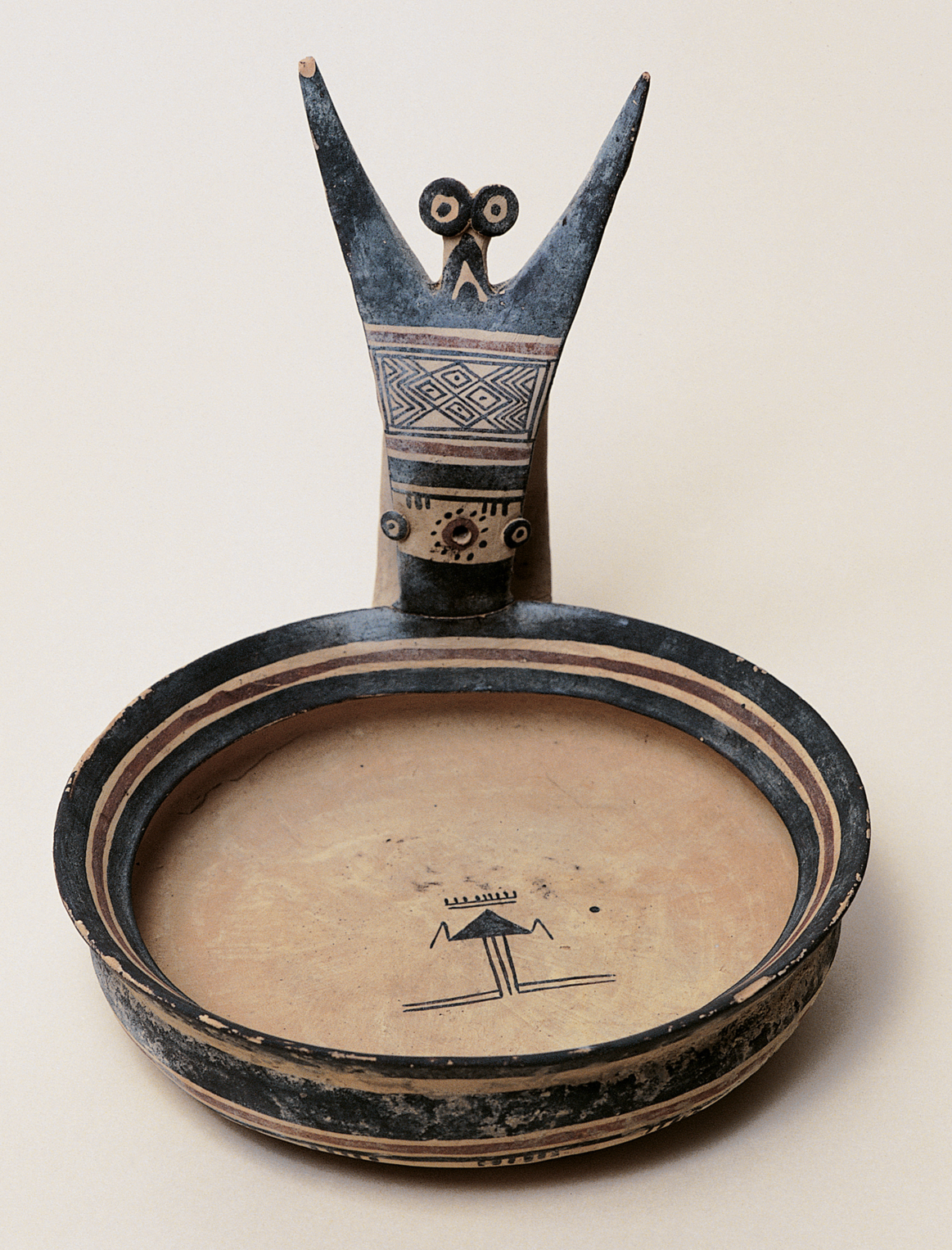 an ancient vessel that looks like a shallow bowl with a geometric human figurine attached