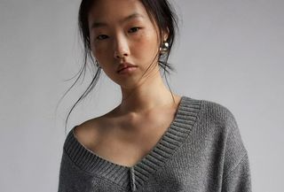 Urban Outiftters model wears v-neck grey knit sweater with silver earrings.