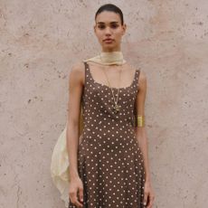 Woman wears yellow scarf, brown polka dot dress, gold jewellery