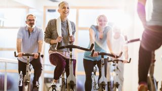 Woman laughing and smiling while holding sweat towel in gym, about to do spinning for weight loss