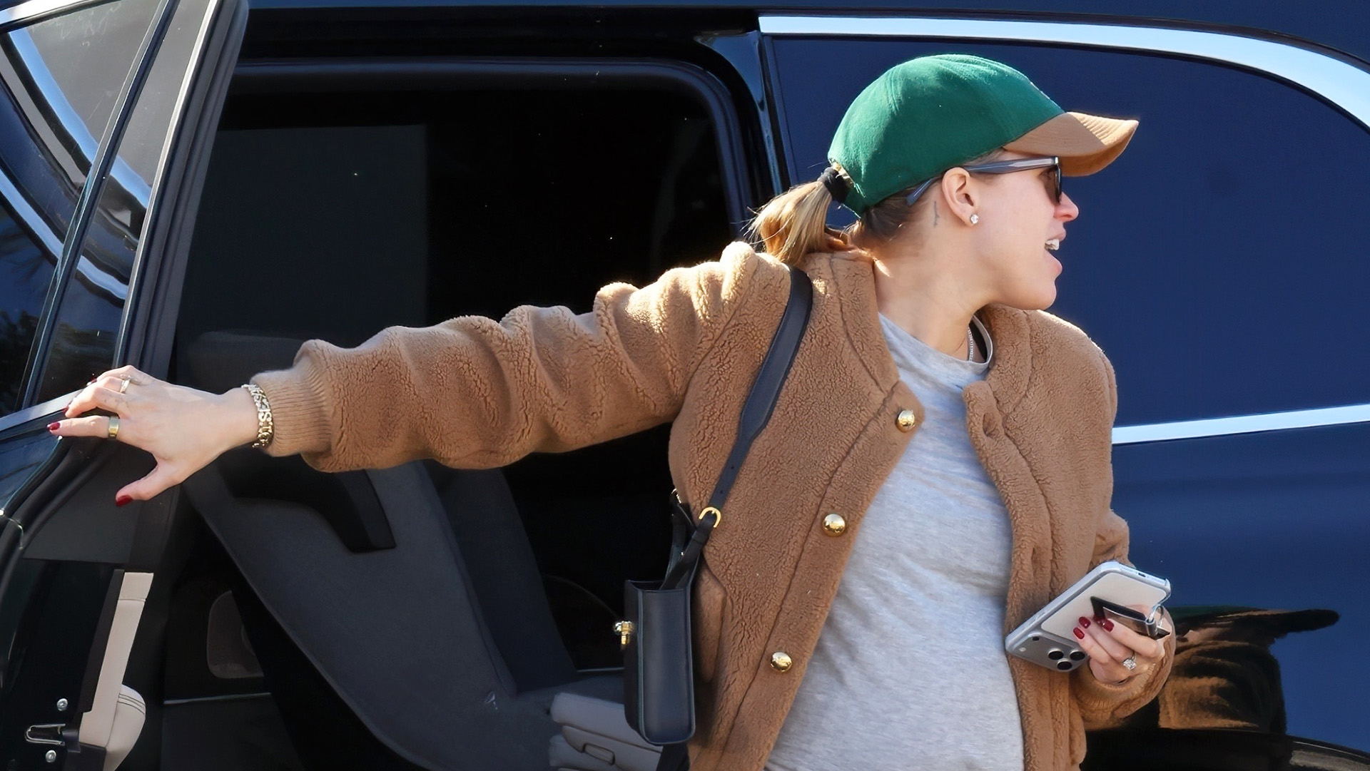 Sofia Richie wearing a camel jacket, gray T-shirt, burgundy pants, a baseball cap, and Uggs