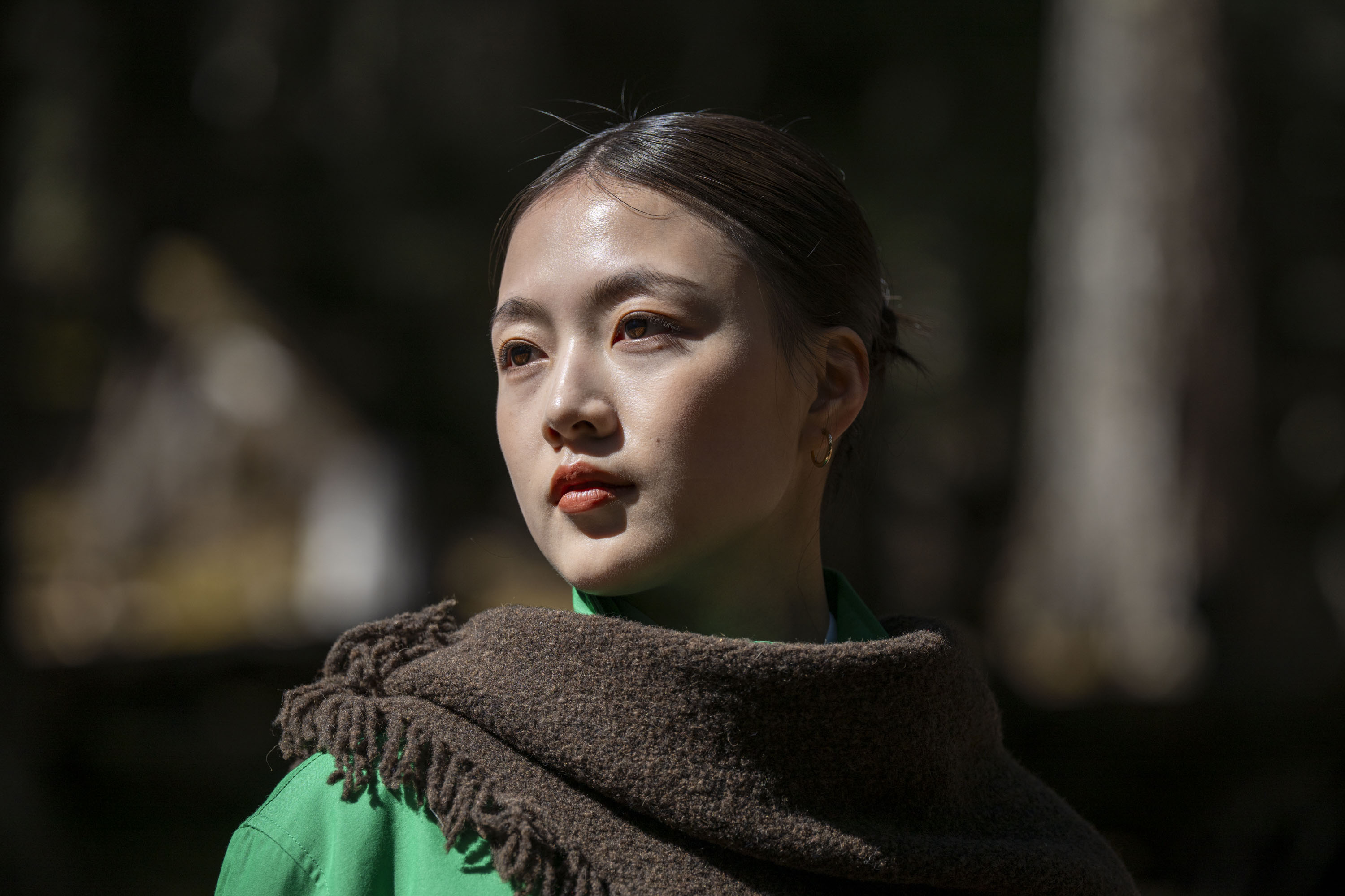 Portrait of a woman in a shawl and green jacket in a woodland, there's direct sunlight on her
