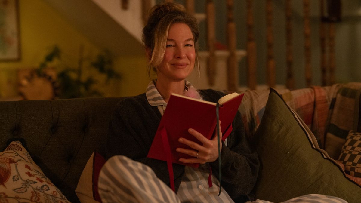 Bridget wearing her pyjamas and sitting on the sofa as she writes in her famous red diary 