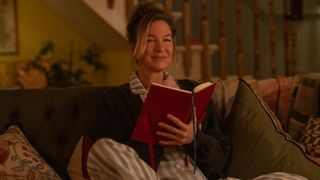 Bridget wearing her pyjamas and sitting on the sofa as she writes in her famous red diary 