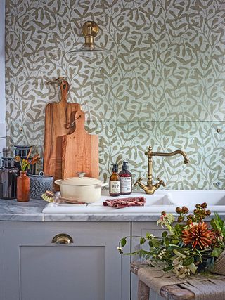 A kitchen sink and marble work top with cutting boards and dish washing tools