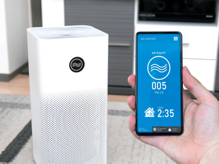 Hand holding a phone with an air quality monitor in front of an air purifier