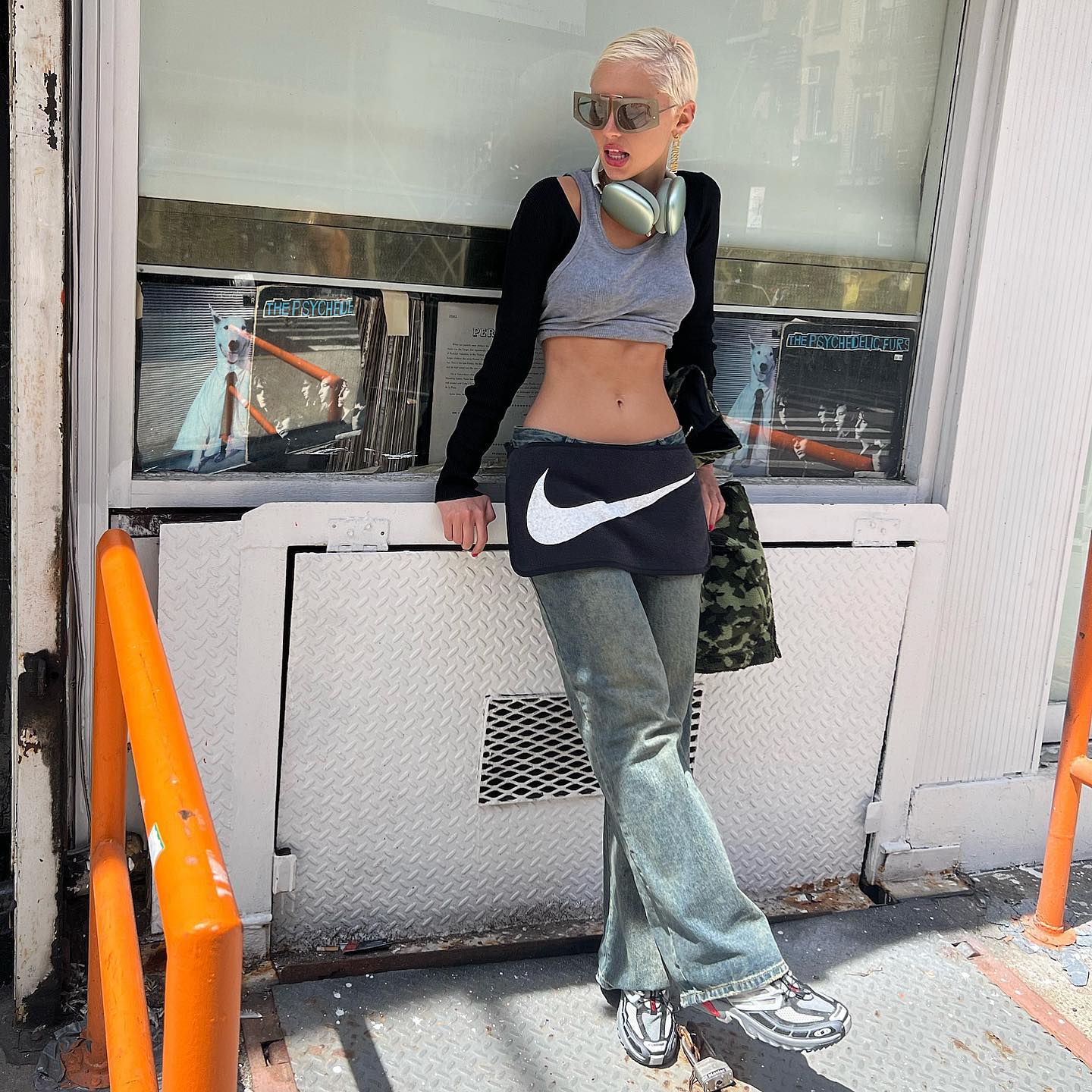 An image of @lirisaw wearing a grey sports bra with a black bolero, vintage Nike mini skirt, flared acid-wash jeans and Nike Shox.