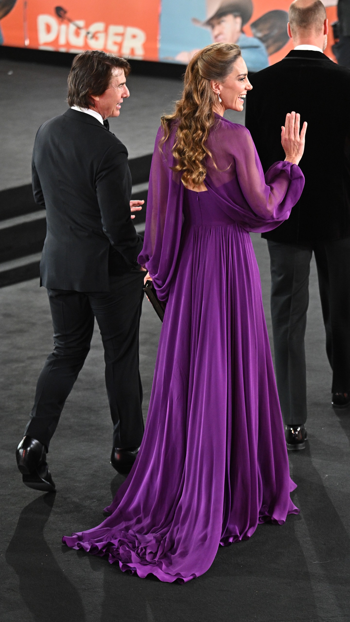 Princess Kate wearing a purple dress and waving walking with Tom Cruise