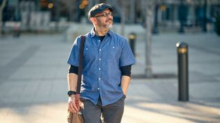 A man wearing a beret walking down a city street in the morning. 